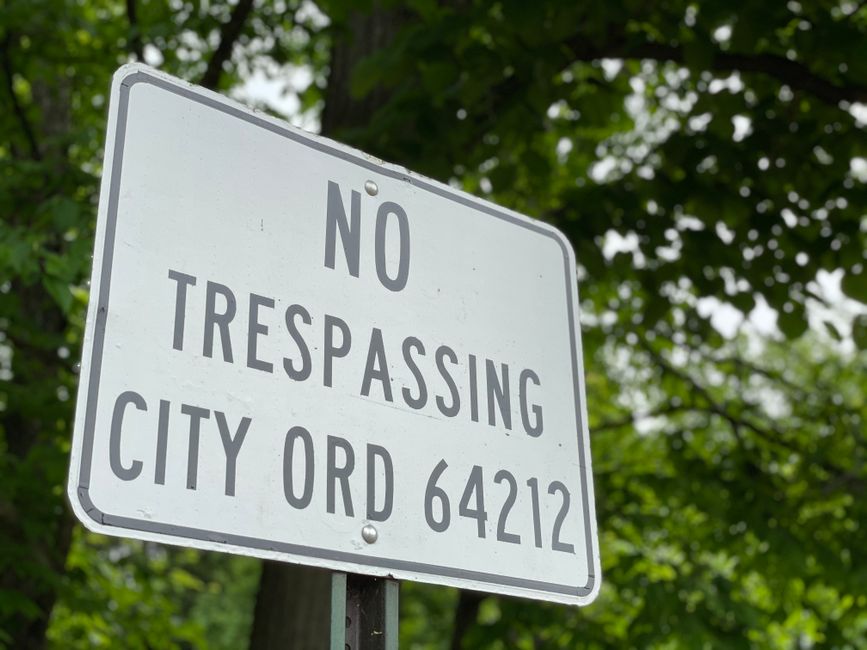 Close-up view of a circular no-parking traffic sign painted on an asphalt surface, featuring a blue circle with a red border and a red diagonal line running from the top left to the bottom right, indicating parking restrictions. The sign appears weathered with some fading and chips in the paint, situated on a grey paved area likely part of a driveway or street on the Forestdale estate. This visual is associated with house removals and moving logistics, as it highlights parking restrictions that can impact home relocation and furniture transport. Forestdale Removals, a professional removal company, would typically need to account for such parking restrictions during the loading process of furniture and boxes into their van. The image underscores the importance of planning for parking regulations when executing successful house removals on estates with parking restrictions.